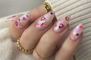 Hand showcasing pink valentines day nails adorned with heart-shaped designs and golden jewelry.